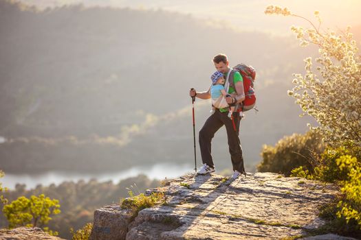 Hiker with baby relaxing standing on cliff against beautiful view