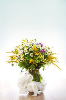 Beautiful bouquet of wildflowers in vase on blue background