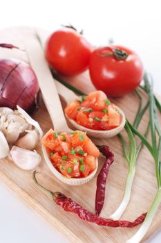 Salsa in two spoons on a wooden board and the ingredients: tomatoes, onions, garlic, chili pepper
