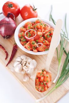 Salsa in a bowl on a wooden board and the ingredients: tomatoes, onions, garlic, chili pepper