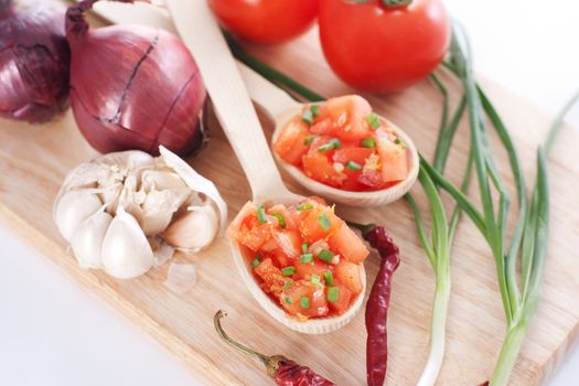 Salsa in two spoons on a wooden board and the ingredients: tomatoes, onions, garlic, chili pepper