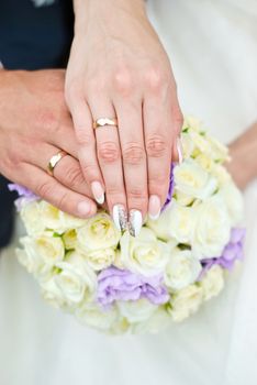 Hands of the groom and the bride with wedding rings on top of the bride's bouquet