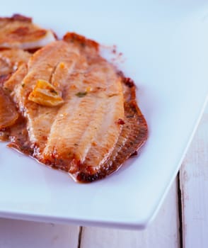 Baked hake over a white plate, with garlic