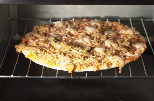 A pizza with tuna warming in an electric oven