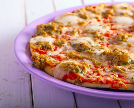 Pizza with tuna over purple plate, white table