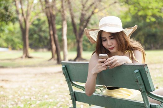 Woman playing smart phone. Sitting on a bench in the park.