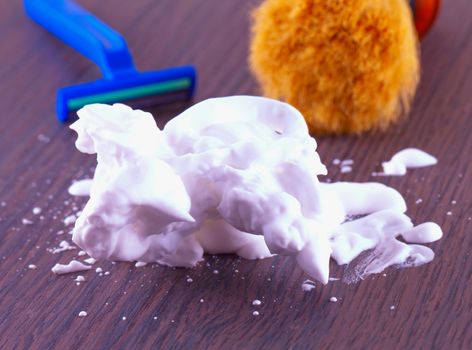 Shaving foam over wooden table, with razor and brush on the back