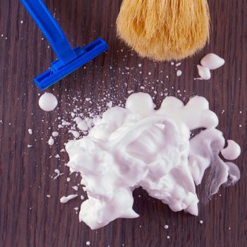 Shaving foam over wooden table, with razor and brush on the back