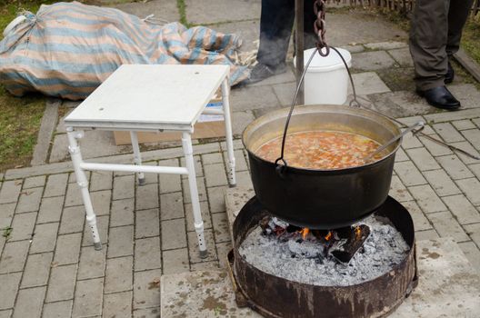 big black metal old pot full of rustic vegetable soup on an open fire outdoors