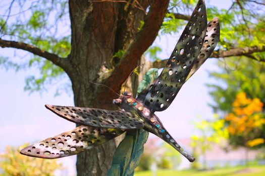 A garden ornament standing by a tree in the shape of a dragonfly insect.
