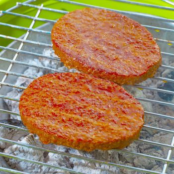 Hamburgers over a bbq, focus over center part of first hamburger