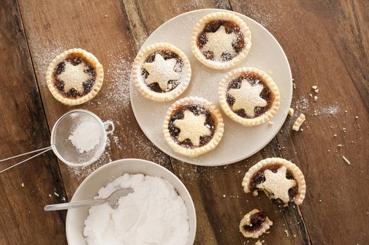 Baking a plate of tasty traditional Christmas mince pies with decorative pastry stars sprinkled with icing sugar, view from above on a wooden kitchen counter