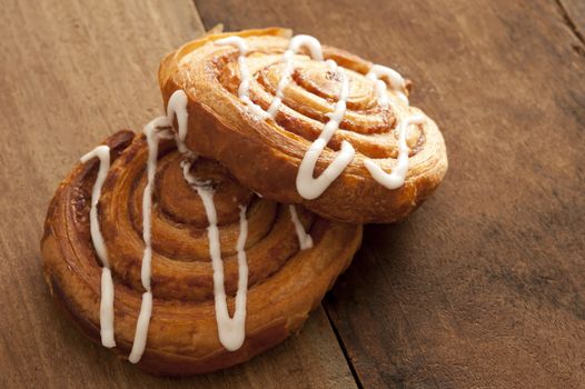 Two delicious freshly baked Danish pastries filled with apple or almond and drizzled with white icing on a rustic wooden kitchen counter ready for a tasty teatime snack