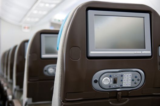 Economy class seats with entertainment system onboard a wide-body airliner. Shallow depth of field with the first seat in focus.