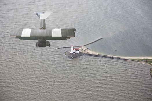 Old airplane flying above water and lighthouse