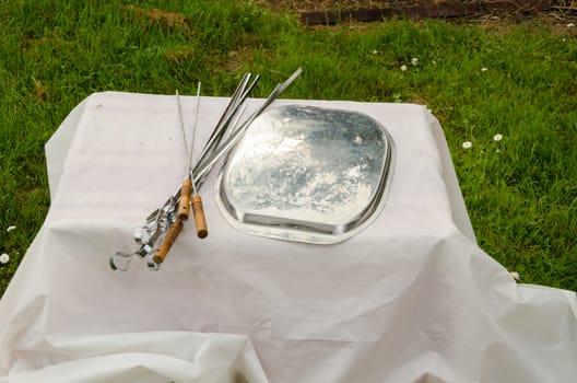 shashlik spits and pad lying on small table with white tablecloth