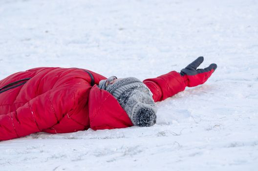 child lie on snow with warm red feather jacket tired from slide outdoors, winter time leisure