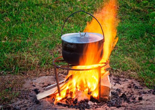 On a green meadow on a burning fire in a pan the food is cooked