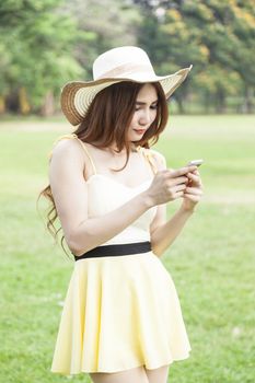 Woman play smart phones. Woman with hat standing in a park with a phone.