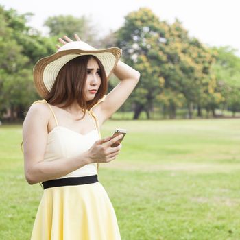 Woman play smart phones. Woman with hat standing in a park with a phone.
