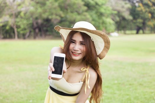 Woman handing the smart phone standing on the grass in the park.