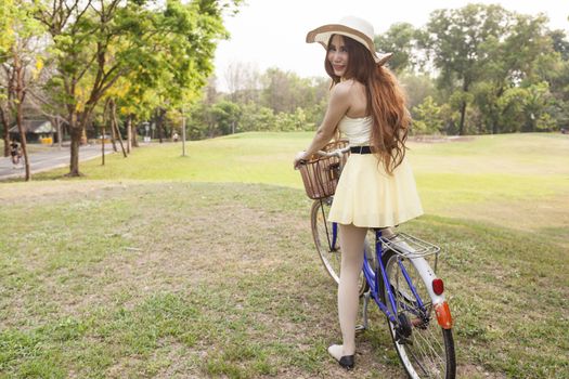 Asian woman riding a bicycle On the grass in the park. Asian woman with long hair wearing a hat.