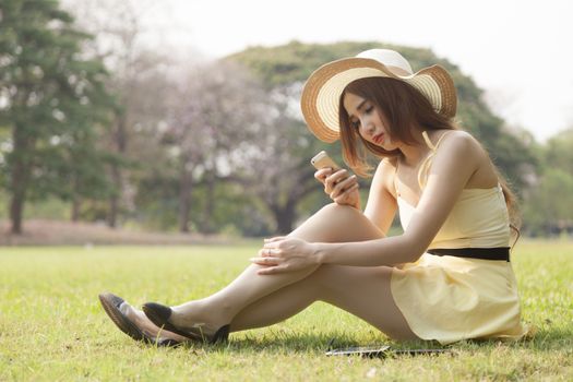 Woman using a phone Sitting on the grass in the park.