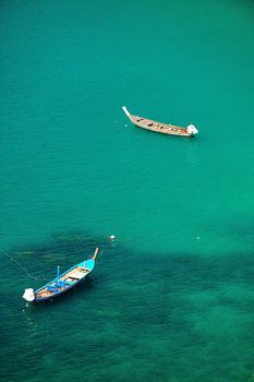 A traditional longtail boat floats in perfect crystal clear emerald blue water. Phuket, thailand