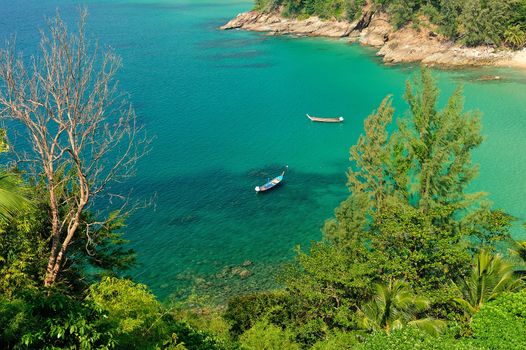 A traditional longtail boat floats in perfect crystal clear emerald blue water. Phuket, thailand