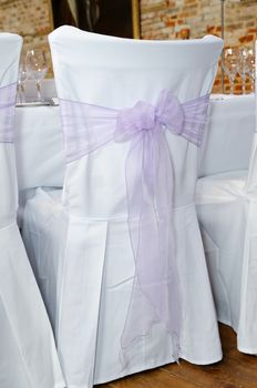 Lilac ribbon in a bow on white chair cover at wedding reception