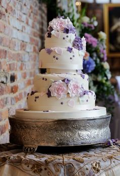 Wedding cake at reception has intricate decoration of pink and purple flowers