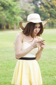 Woman play smart phones. Woman with hat standing in a park with a phone.