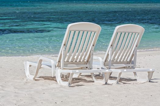 Two white sunbeds on a sandy beach facing the Caribbean Sea.