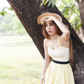 Portrait Asian woman in the park. Under a tree and looking out ahead of her.