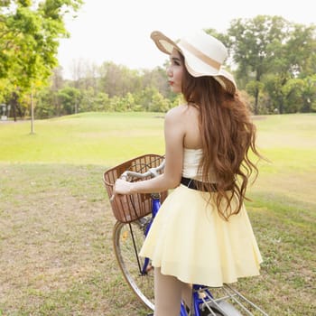 Asian woman riding a bicycle On the grass in the park. Asian woman with long hair wearing a hat.