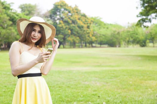 Woman play smart phones. Woman with hat standing in a park with a phone.