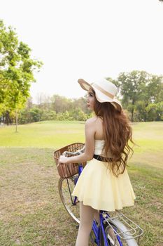 Asian woman riding a bicycle On the grass in the park. Asian woman with long hair wearing a hat.