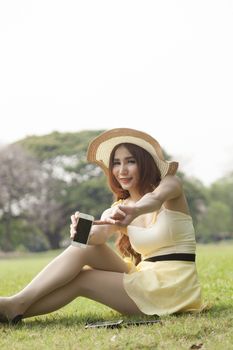 Woman filing phone. Sitting on the grass in the park.