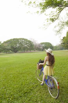 Woman riding a bicycle. Woman with hat riding a bicycle in the park.