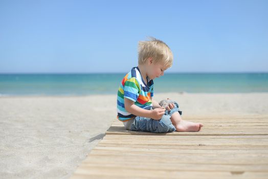 Small boy sitting on a wooden walkway on the beach
