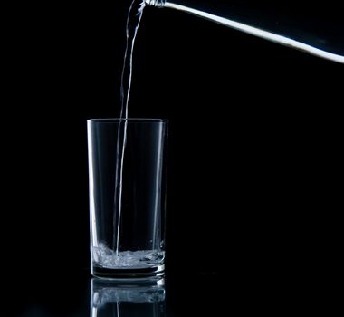 Pouring water on glass on over black background