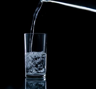 Pouring water on glass on over black background