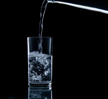 Pouring water on glass on over black background