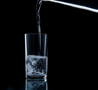 Pouring water on glass on over black background