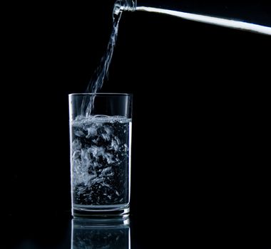 Pouring water on glass on over black background