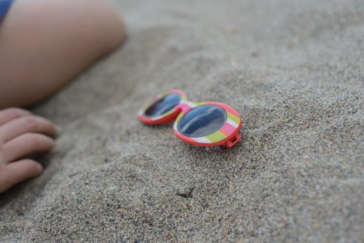 Striped sunglasses with body parts in the sand
