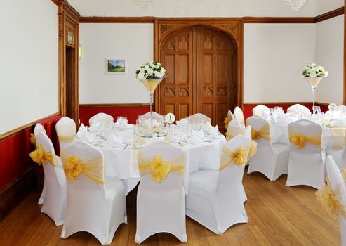 Wedding reception setting showing white floral arrangement and yellow chair cover with bow