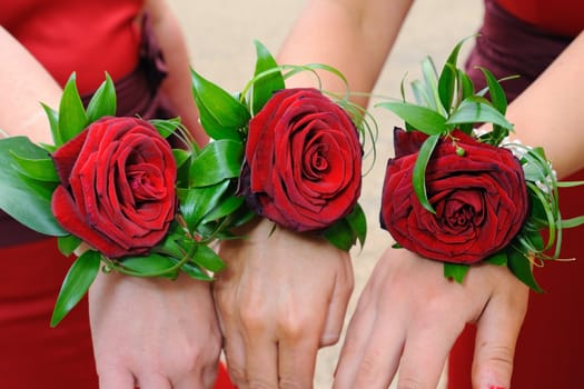Three red roses worn on bridesmaids wrists.