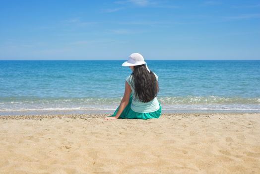 Brunette female with long hair sitting alone on the sandy beach