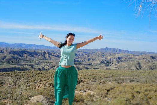 Young happy woman open arms stand at mountain